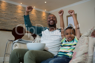 Excited father and son watching football match in living room