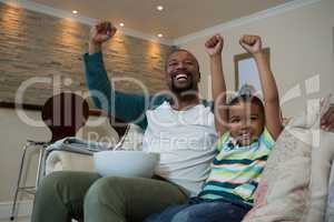 Excited father and son watching football match in living room