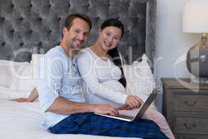 Happy couple using laptop in bedroom