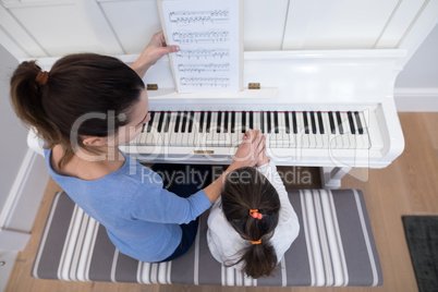 Overhead of mother assisting daughter in playing piano