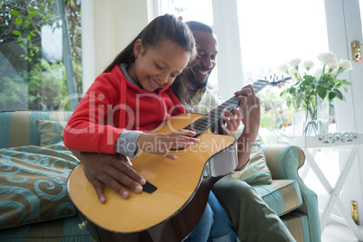 Father and daughter playing guitar together in living room