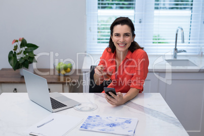 Woman using mobile phone while having lemon tea in kitchen