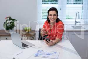 Woman using mobile phone while having lemon tea in kitchen
