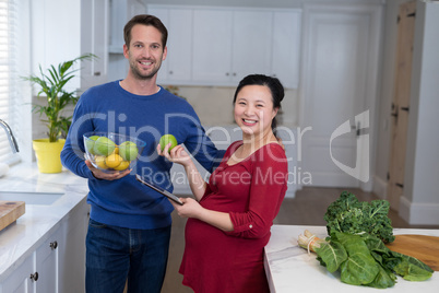 Pregnant couple holding sweet limes and digital tablet in the kitchen
