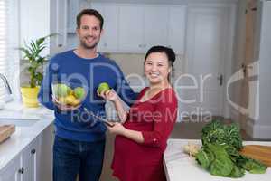 Pregnant couple holding sweet limes and digital tablet in the kitchen