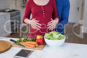 Man touching womans pregnant belly in the kitchen