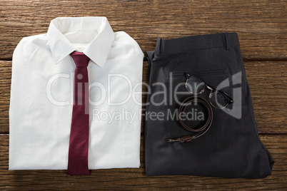 Folded school uniform, belt and spectacle on wooden plank
