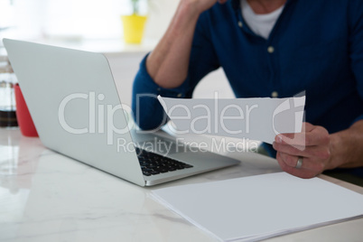 Mid section of man holding bill in kitchen