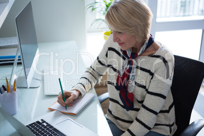 Beautiful woman writing in organizer while using laptop