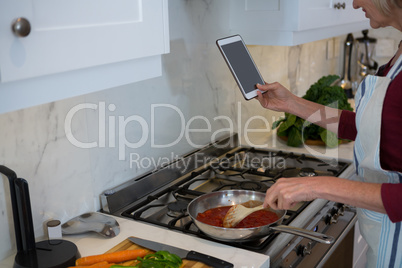 Woman using digital tablet while cooking food