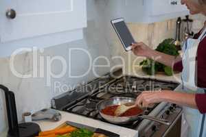 Woman using digital tablet while cooking food
