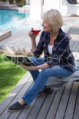 Beautiful woman reading book while drinking wine in porch