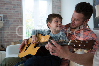 Father assisting his son in playing guitar