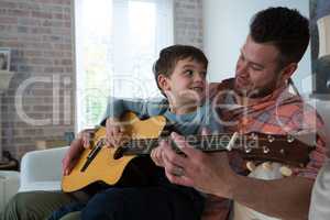 Father assisting his son in playing guitar