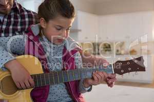 Father assisting his daughter in playing guitar