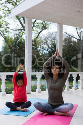 Mother and daughter meditating together in the porch
