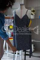 Female designer measuring the length of dress on mannequin