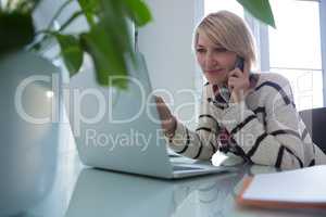 Woman talking on mobile phone while using laptop