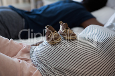 Pregnant woman relaxing with baby shoes on her belly in bedroom