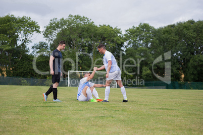 Football player assisting his friend to get up