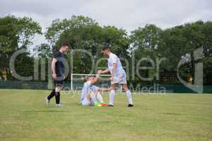 Football player assisting his friend to get up