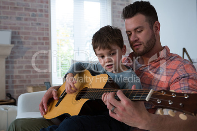 Father assisting his son in playing guitar