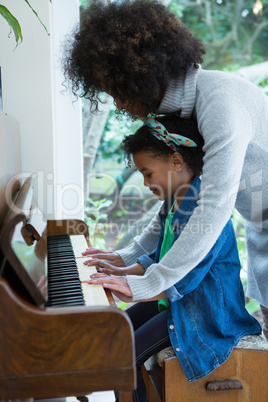 Mother assisting daughter in playing piano