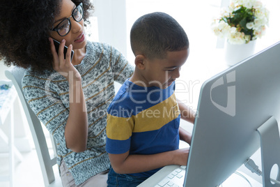 Mother talking on mobile phone while son using computer