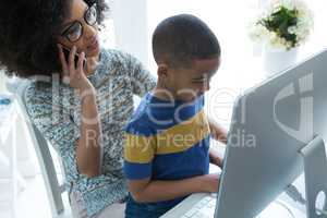 Mother talking on mobile phone while son using computer