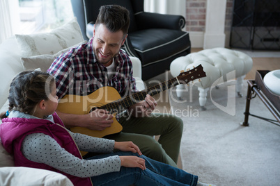 Father assisting his daughter in playing guitar