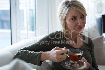 Thoughtful woman having lemon tea in living room