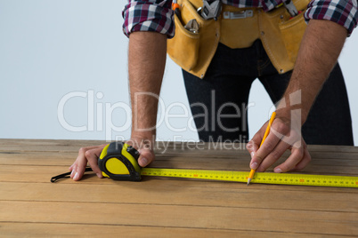 Male architect measuring wooden plank with tape measure