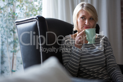 Thoughtful woman having coffee in living room