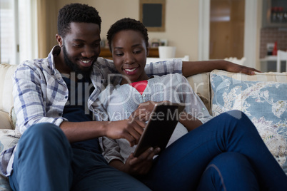 Couple using digital tablet in living room