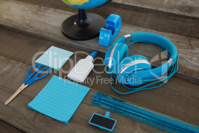 Headphone and globe with various stationery on wooden surface