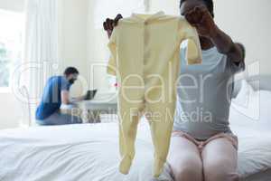 Pregnant woman holding baby clothes in bedroom