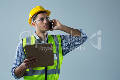 Male architect holding clipboard and talking on mobile phone