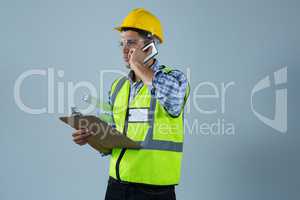 Male architect holding clipboard and talking on mobile phone