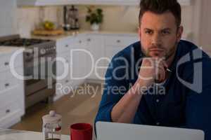 Thoughtful man sitting at table with laptop