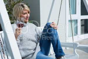 Thoughtful woman having wine in porch