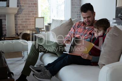 Father ans son reading book in living room