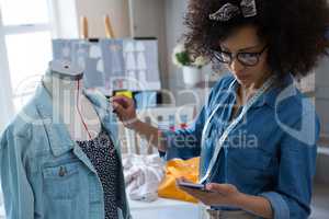 Female fashion designer using mobile phone while designing dress