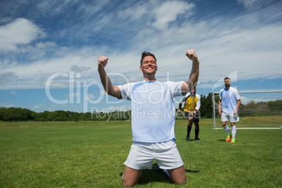 Excited football player in celebrating scoring goal kneeling on grass pitch