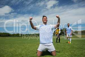 Excited football player in celebrating scoring goal kneeling on grass pitch