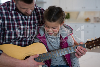 Father assisting his daughter in playing guitar