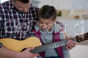 Father assisting his daughter in playing guitar