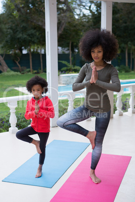Mother and daughter performing yoga in the porch