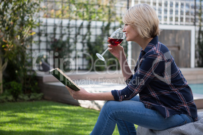 Beautiful woman reading book while drinking wine in porch