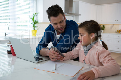 Father and daughter using mobile phone at table