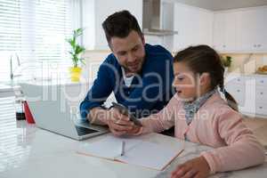 Father and daughter using mobile phone at table